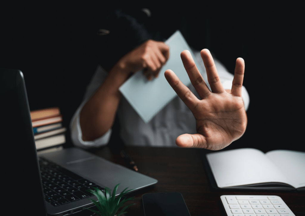 Femme qui se cache derrière une feuille à son bureau et qui tend la main pour faire cesser le harcelement au travail qu'elle subit